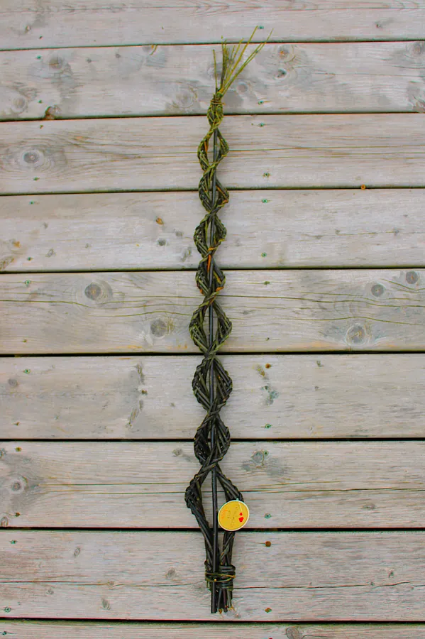 A tall double-spiral willow wand woven around straight rods, on weathered barnboard