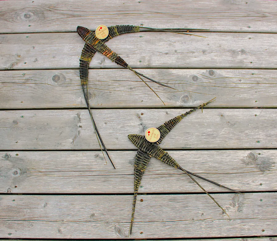 A pair of swallows in flight, woven from dark and green willow, resting on weathered barnboard